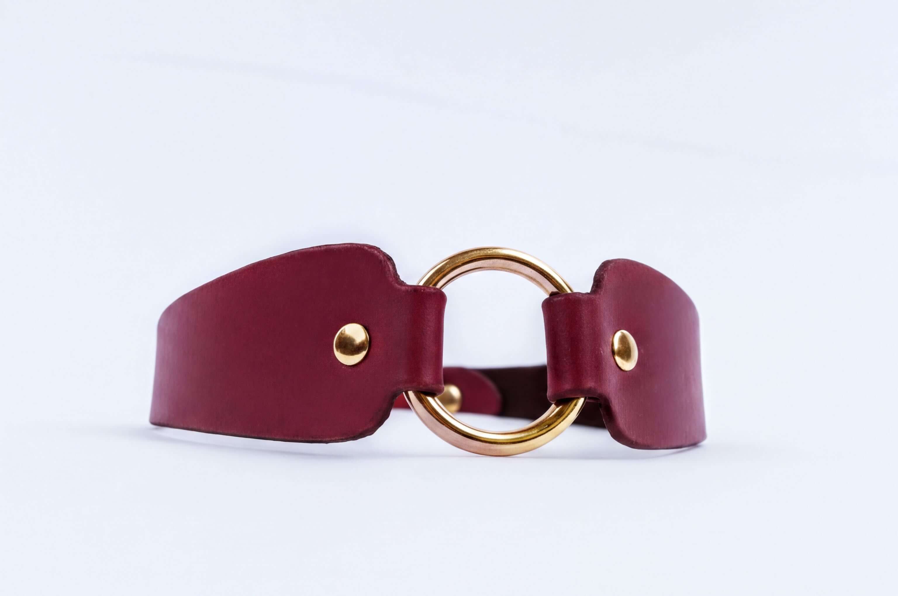 A burgundy leather choker necklace with a gold-colored circular buckle.