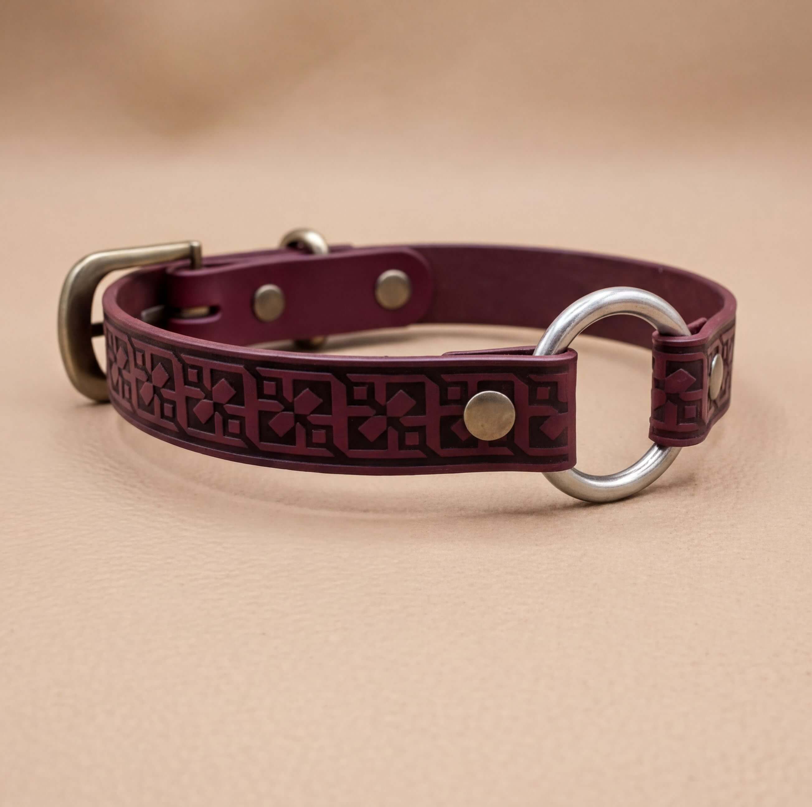 A burgundy leather dog collar with a metal ring and buckle, featuring a decorative pattern on the leather.