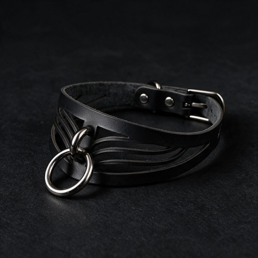 A black leather choker necklace with metal rings and a buckle is shown against a dark background.