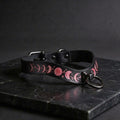 A black leather collar with a pink moon and star design on it, resting on a dark surface.