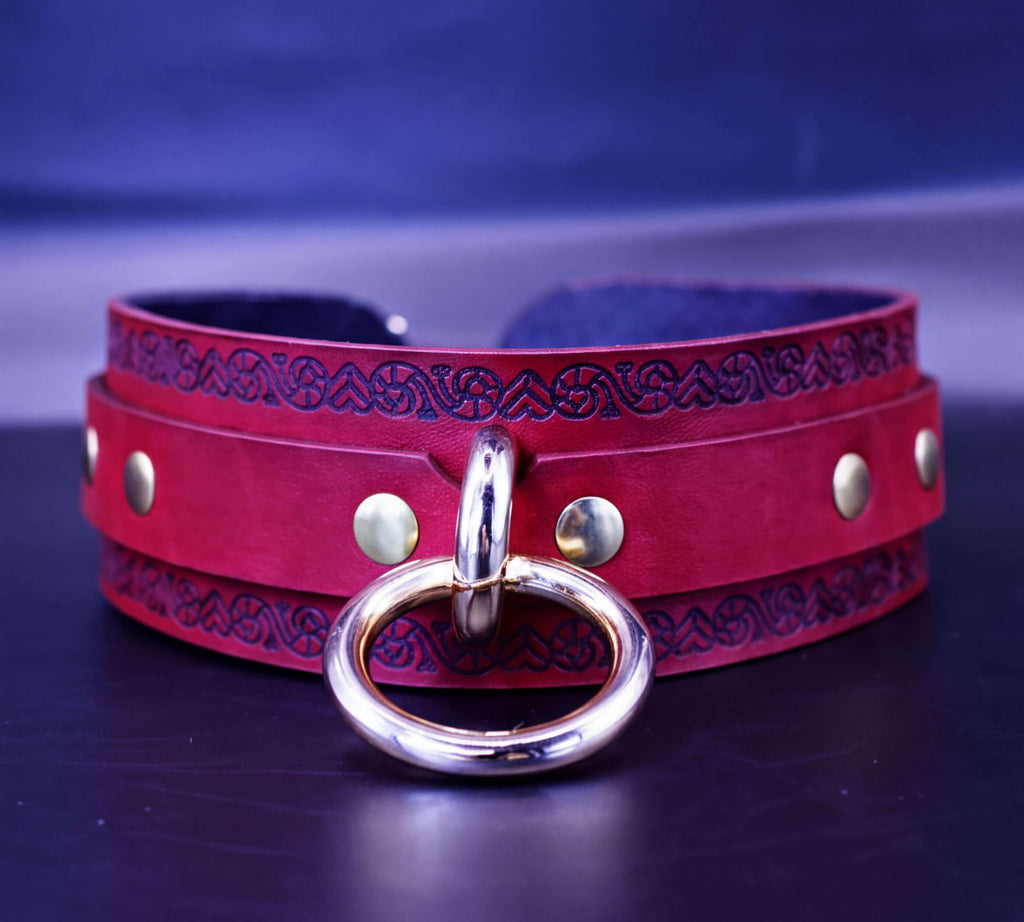 A red leather choker necklace with a gold-colored metal ring and decorative patterns on the band.
