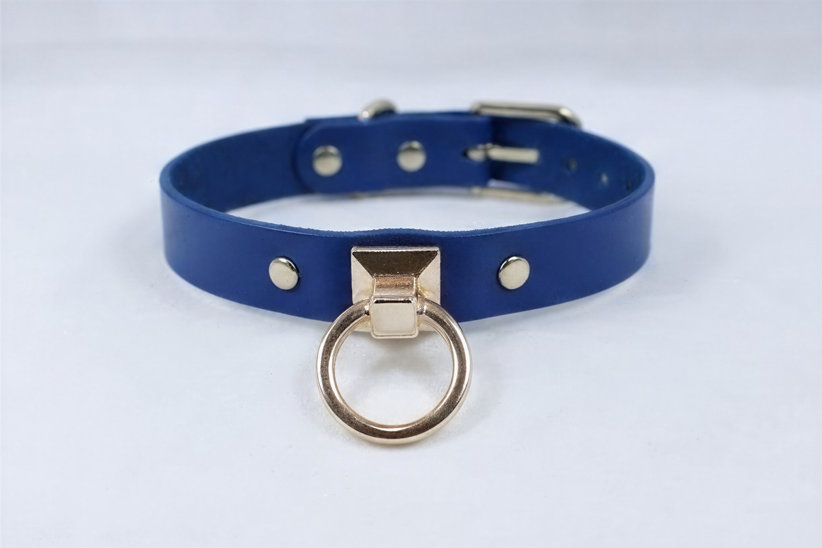 A blue leather choker necklace with a gold-colored metal ring and three small gold-colored studs on the collar.