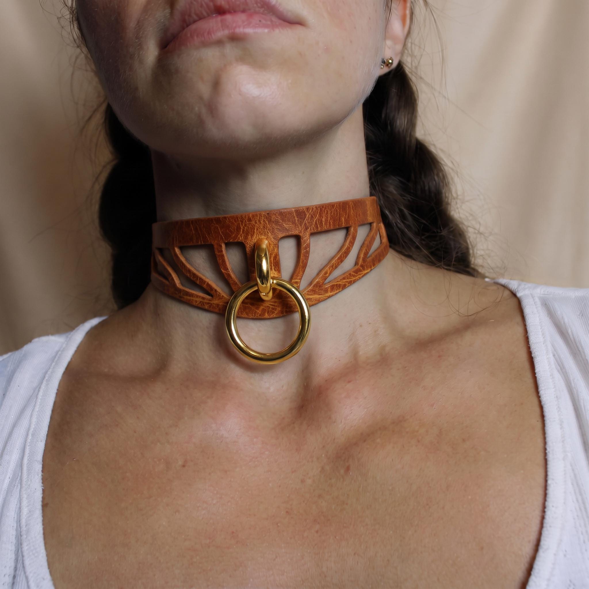 A close-up of a woman's neck and chest area, featuring a choker-style leather necklace with a gold ring.