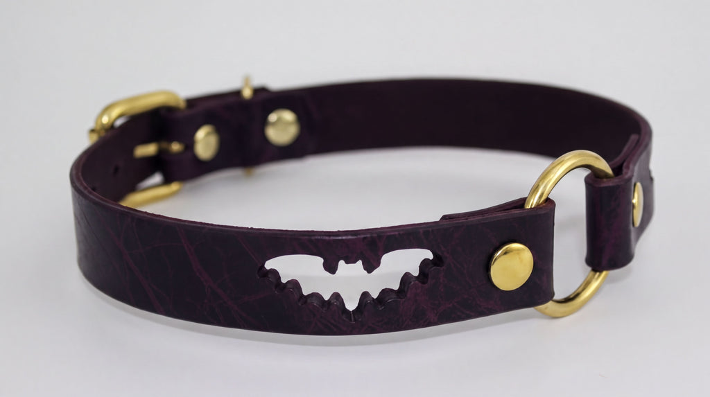 A burgundy leather dog collar with a bat-shaped cutout and gold-colored buckles.