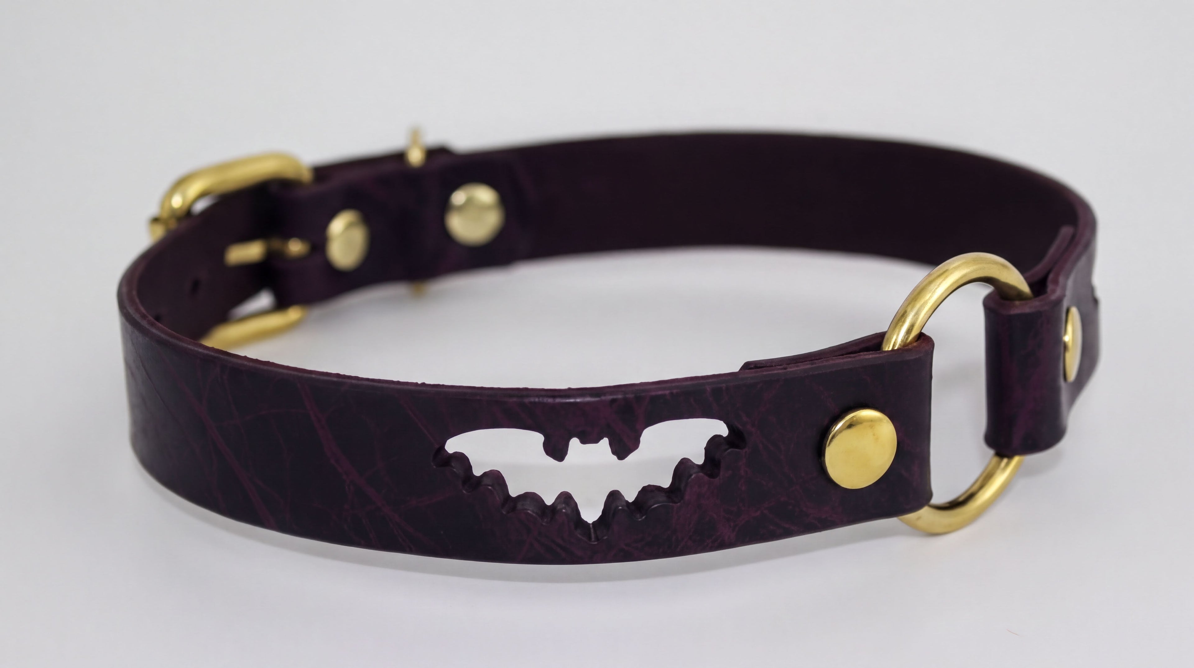 A burgundy leather dog collar with a bat-shaped cutout and gold-colored buckles.