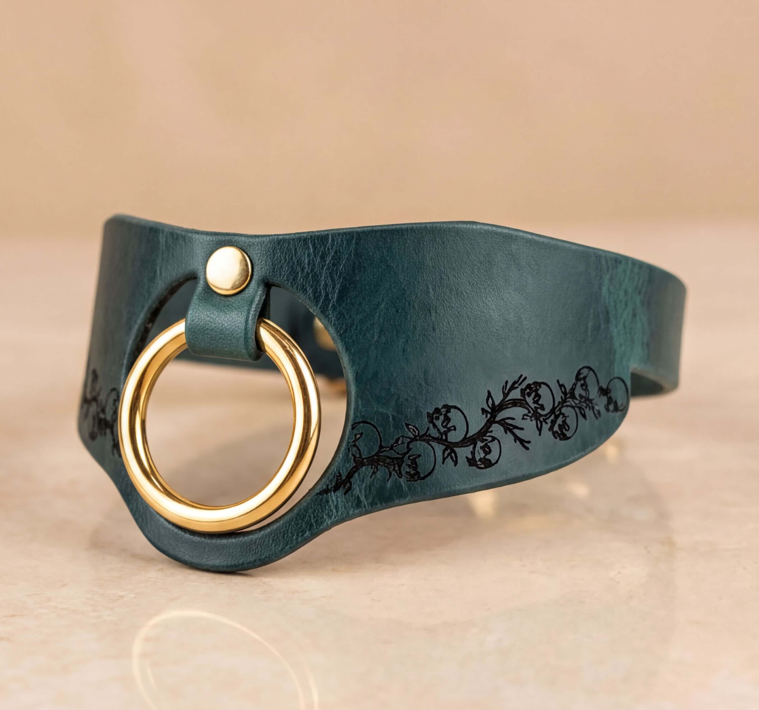 A dark green leather choker necklace with a gold-colored ring and a floral design on the side.