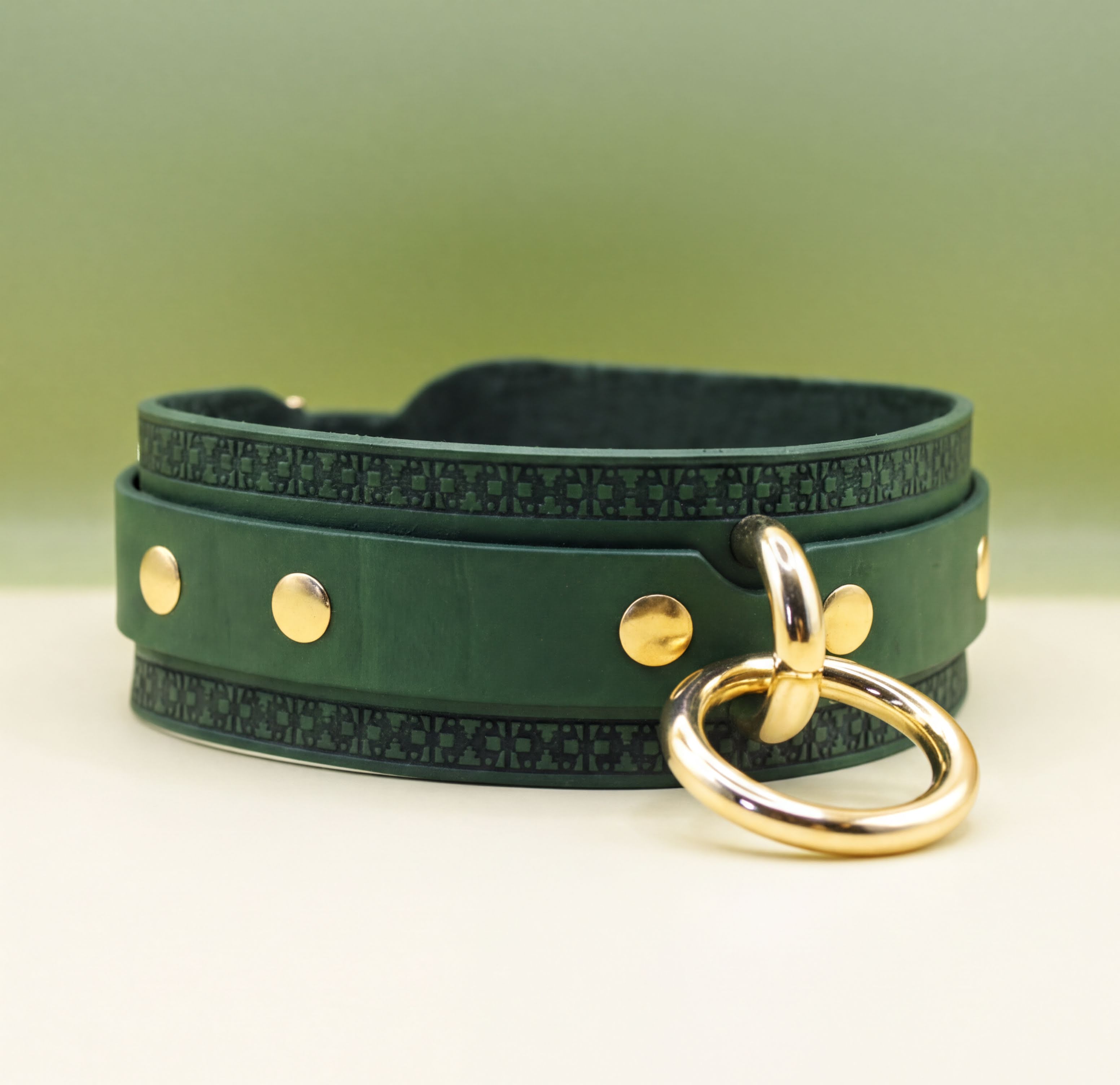 A green leather choker necklace with gold metal rings and a gold ring hanging from it.
