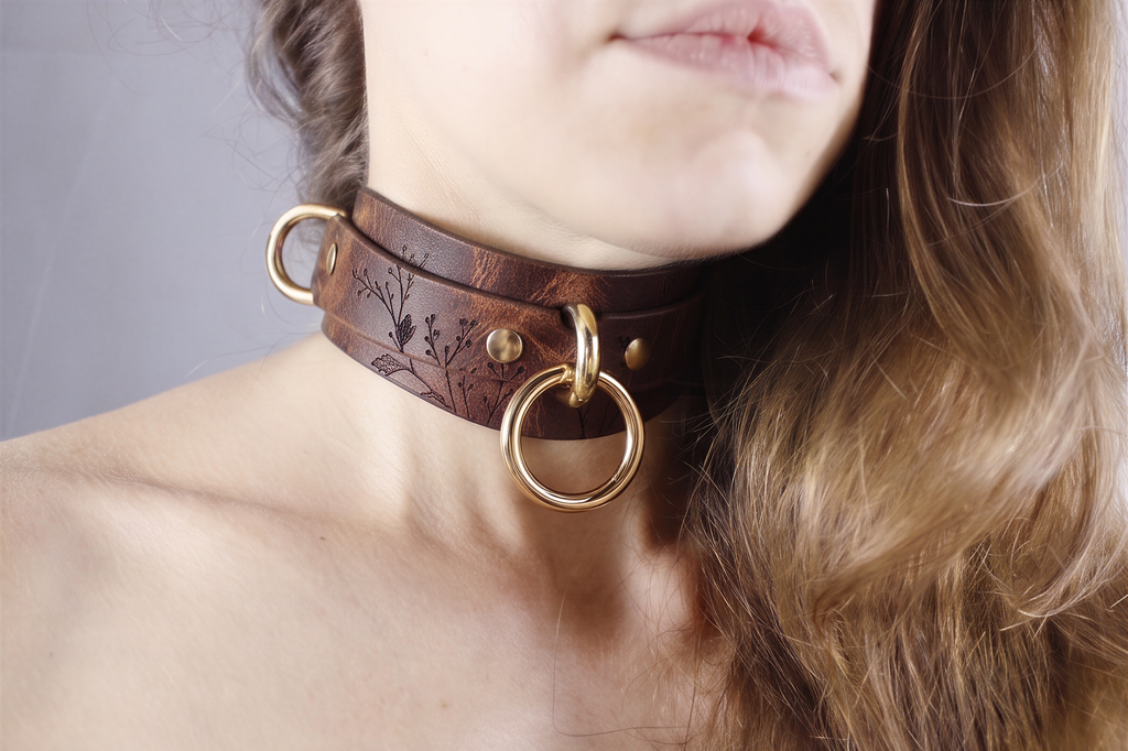 A close-up of a woman's neck and chin wearing a brown leather choker necklace with gold rings.