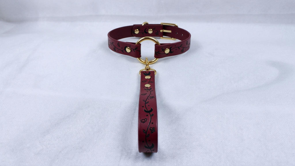 A burgundy leather collar with a gold-colored buckle and a floral pattern on the strap.