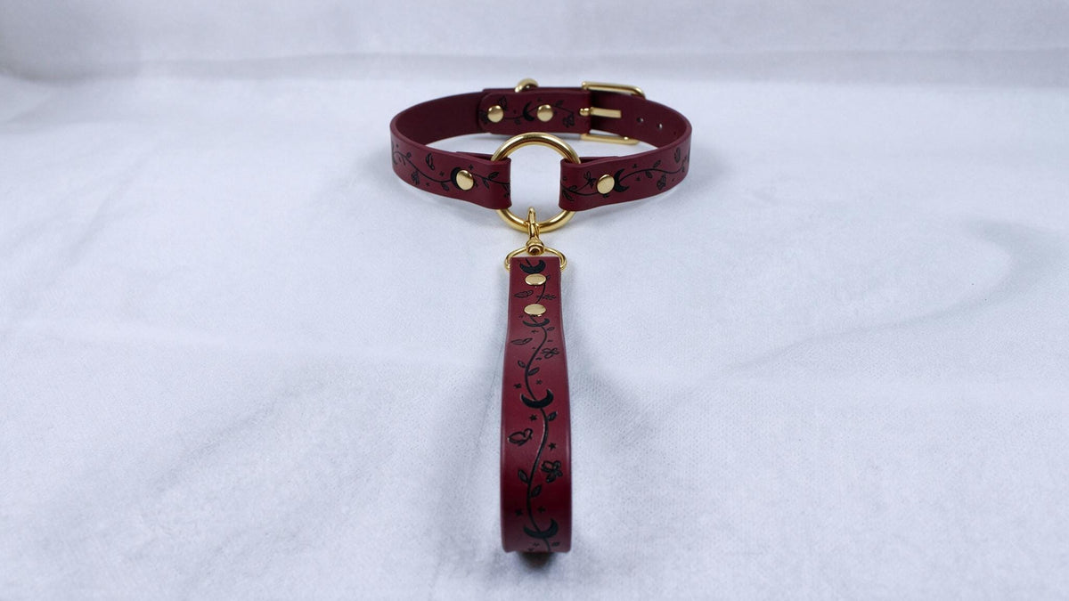 A burgundy leather collar with a gold-colored buckle and a floral pattern on the strap.