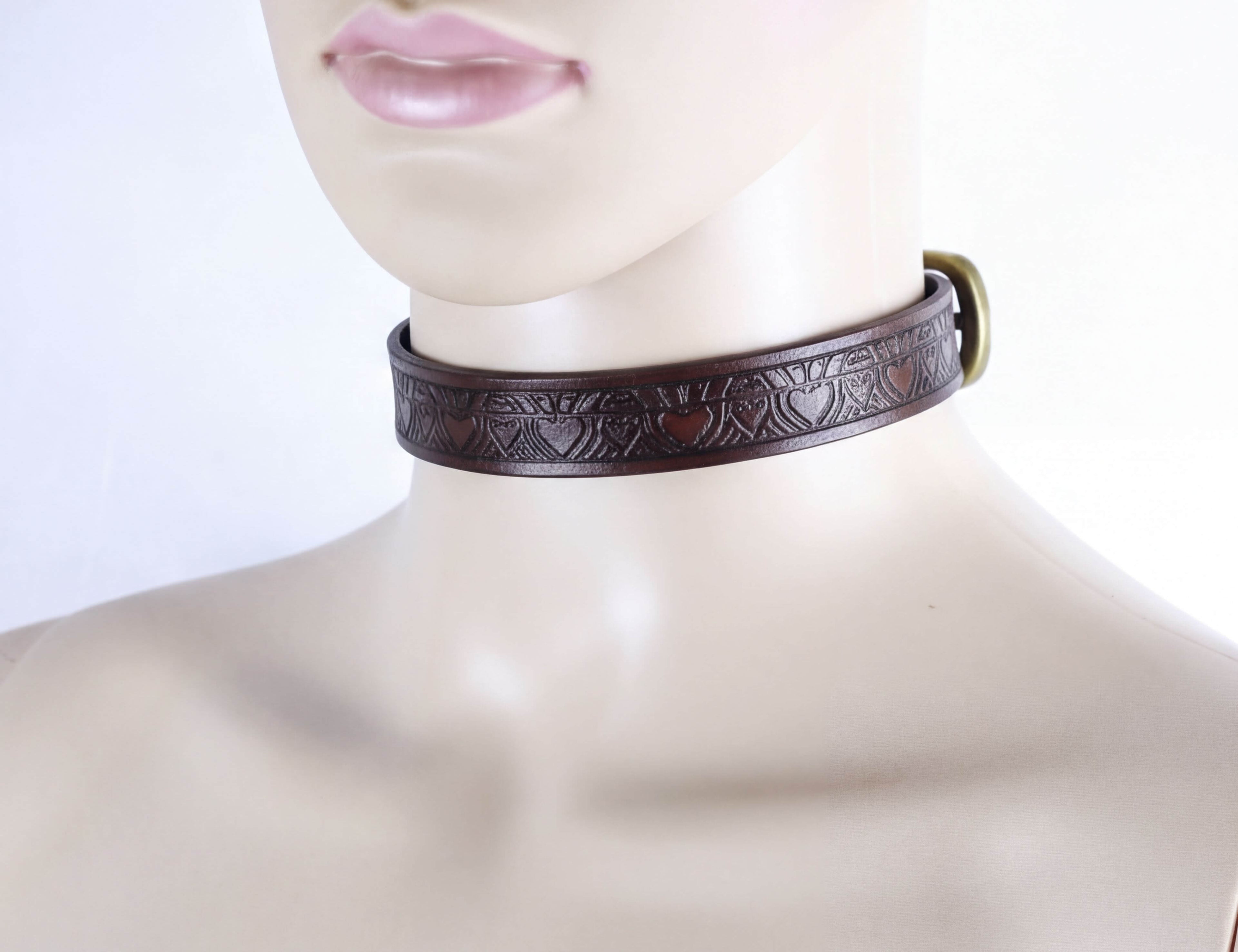 A close-up of a mannequin head wearing a brown leather choker necklace with a decorative pattern.