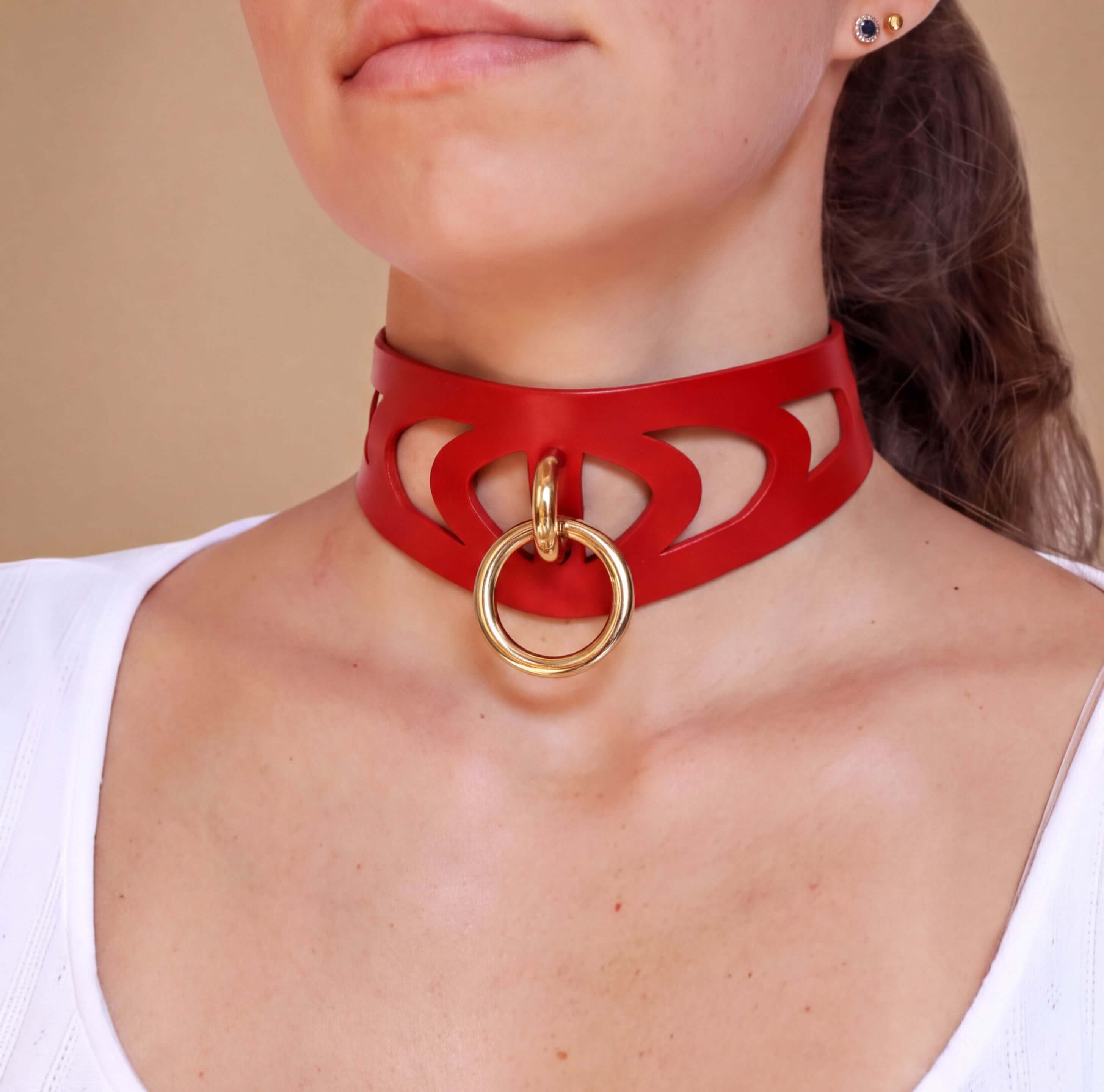 A close-up of a woman wearing a red choker necklace with a gold ring on it.