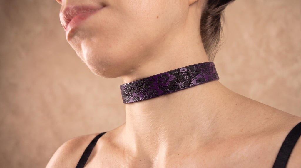 A close-up of a woman's neck and chest area wearing a purple choker necklace with a floral pattern.