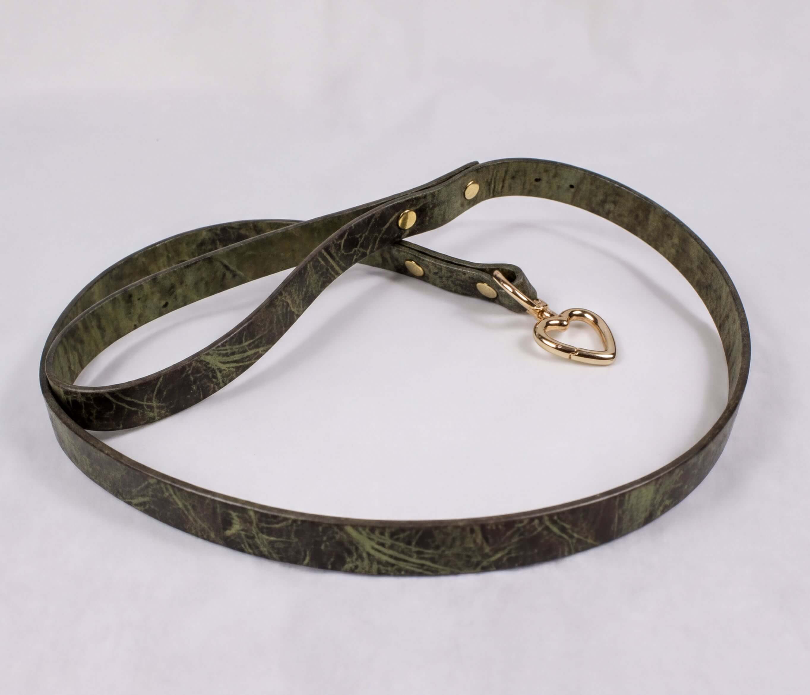 A green leather belt with a heart-shaped charm attached, lying on a white surface.