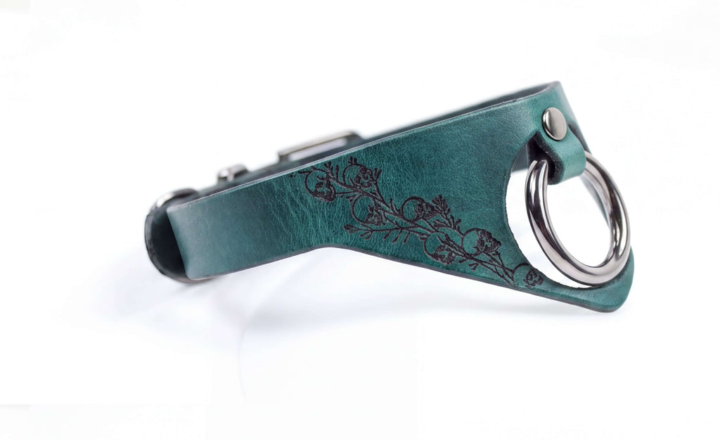 A close-up view of a green leather collar with a metal ring and a floral design on the side.