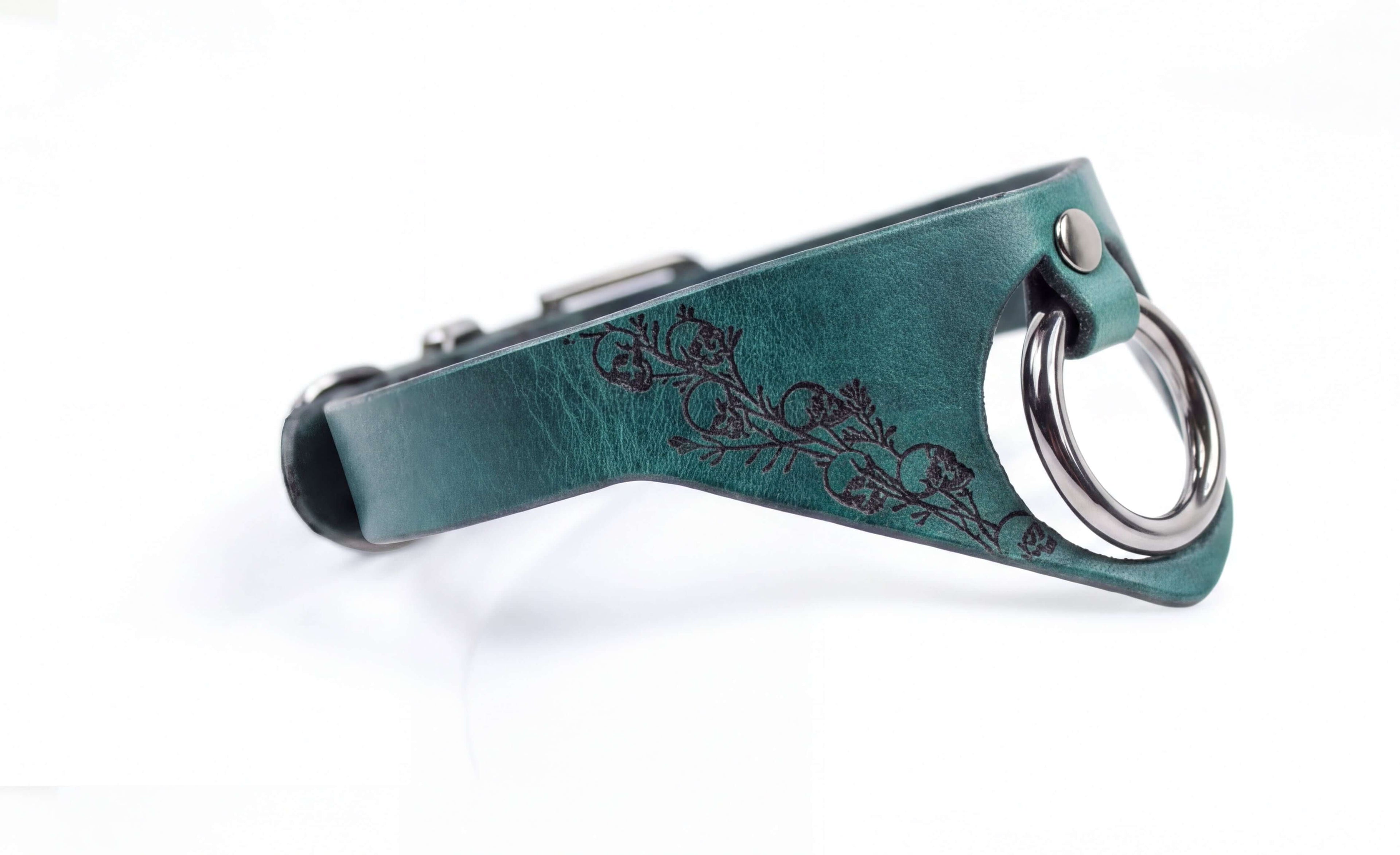 A close-up view of a green leather collar with a metal ring and a floral design on the side.