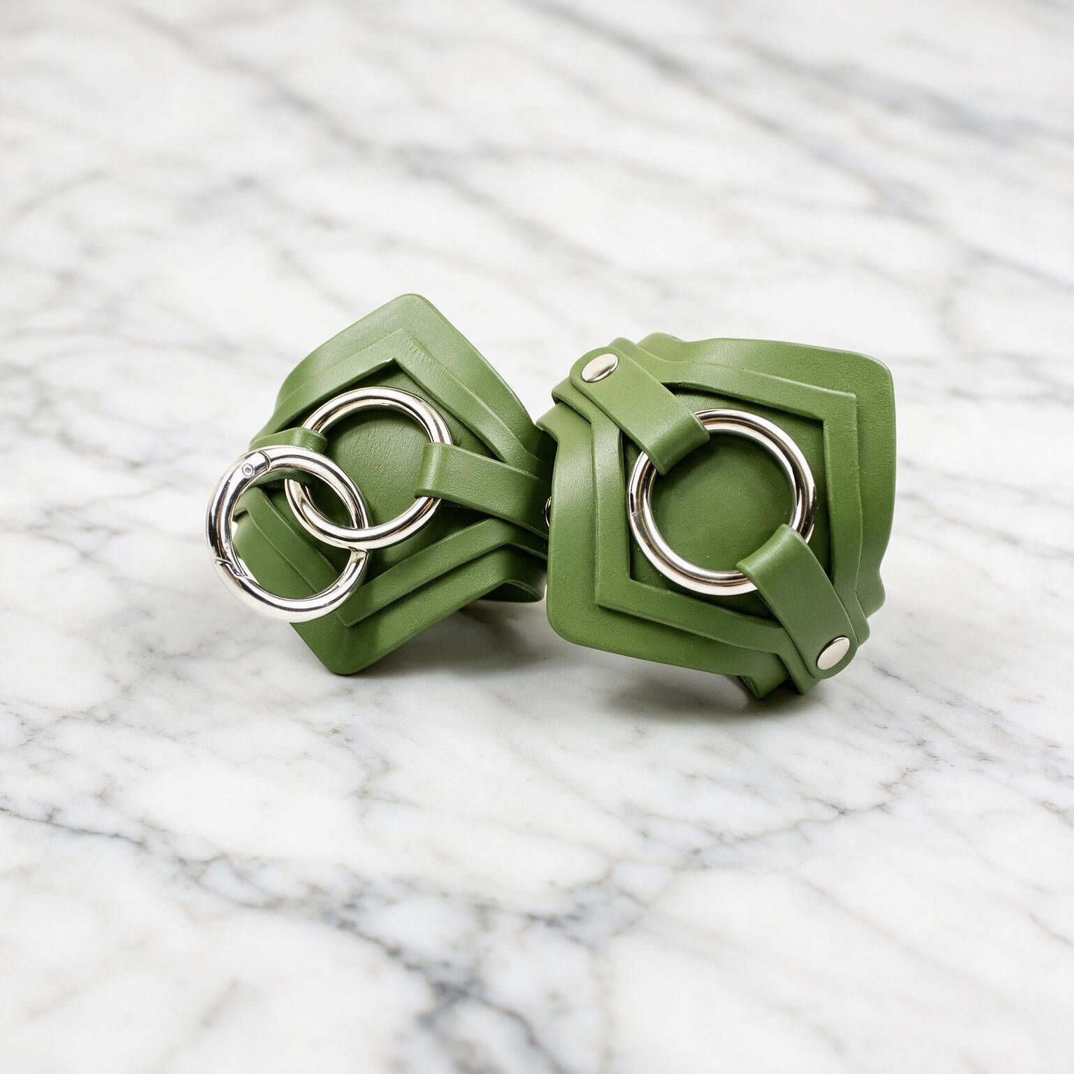 a pair of green leather straps with metal rings, resting on a marble surface.