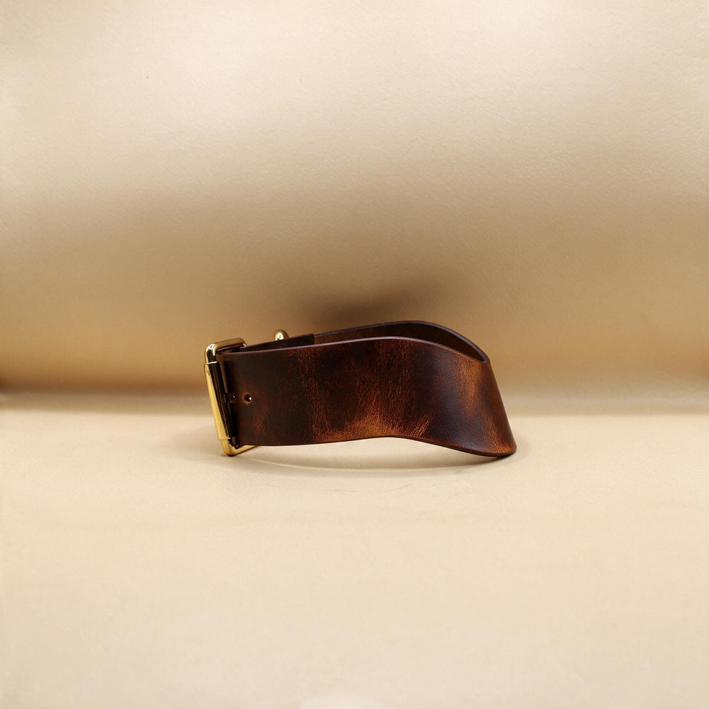 A brown leather belt with a gold buckle is shown against a beige background.