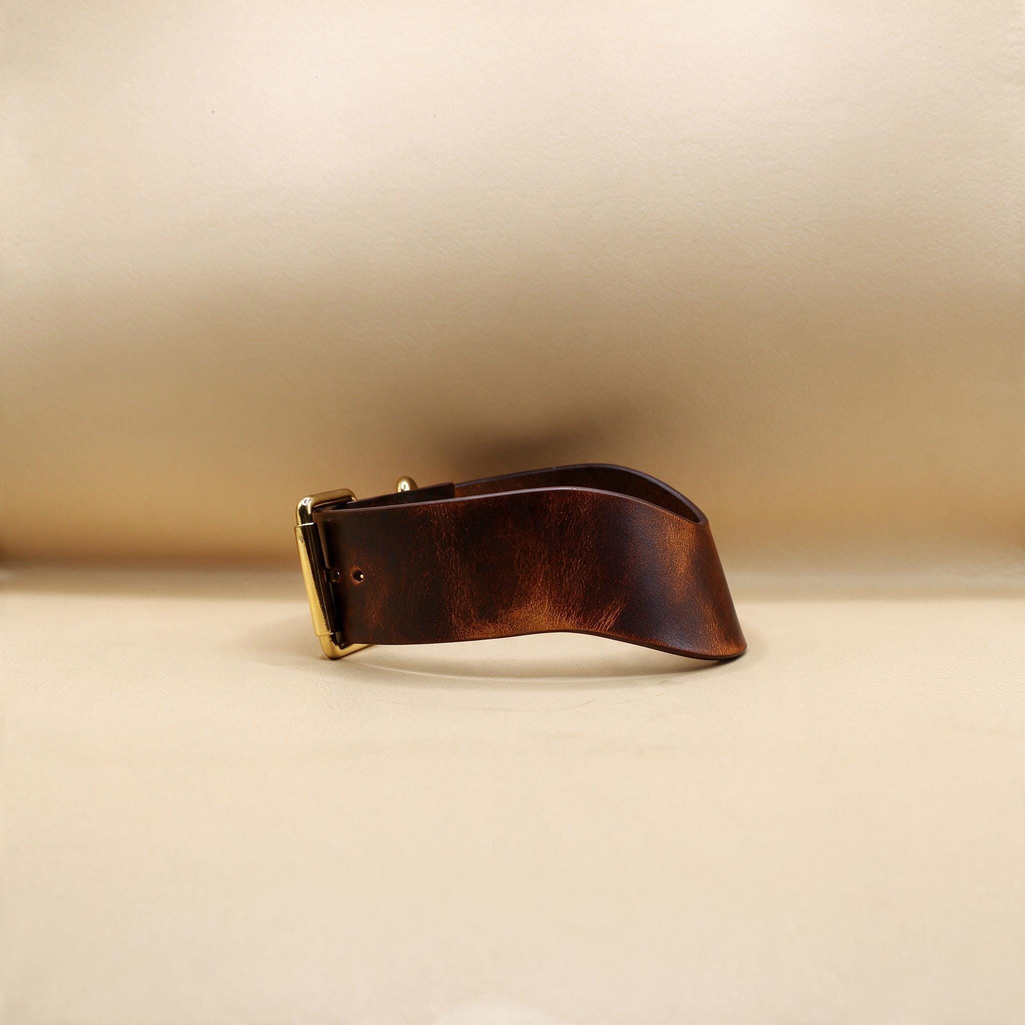 A brown leather belt with a gold buckle is shown against a beige background.