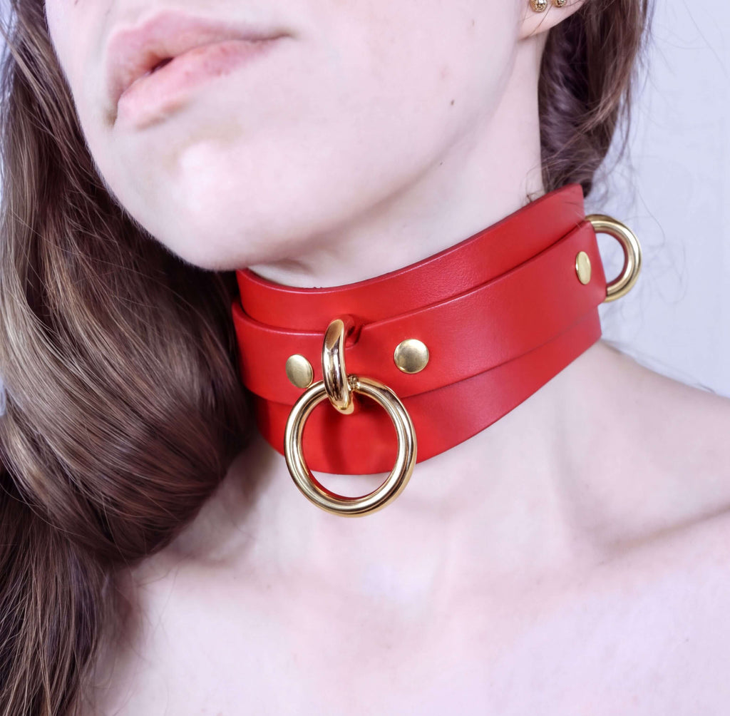 A close-up of a person's neck wearing a red leather choker with gold hardware.