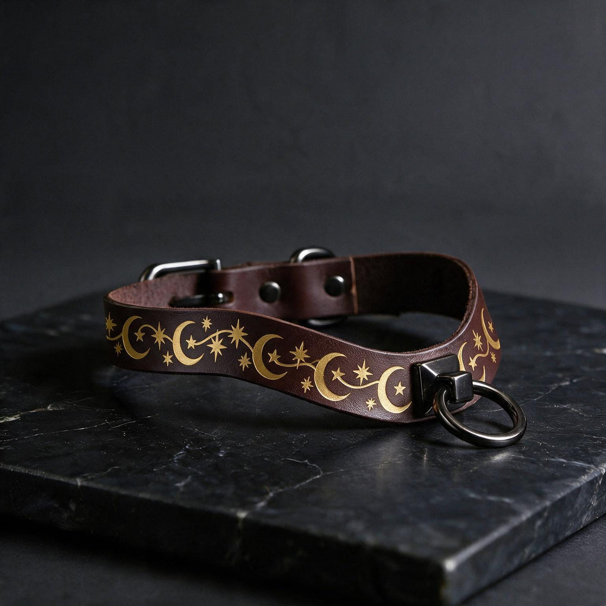 A brown leather collar with a star and crescent design on it, resting on a black surface.