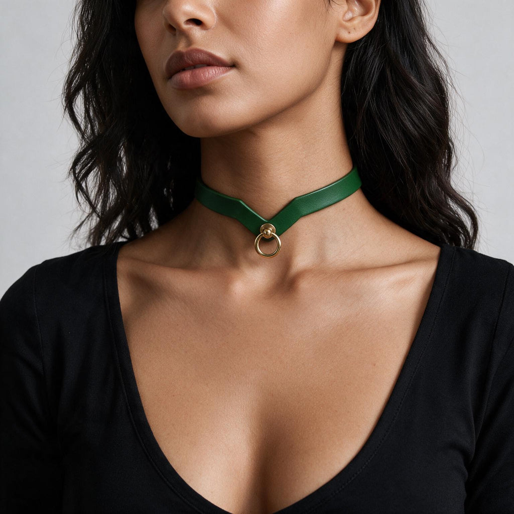 A close-up of a woman's neck and chest area wearing a green choker necklace with a gold-colored ring.