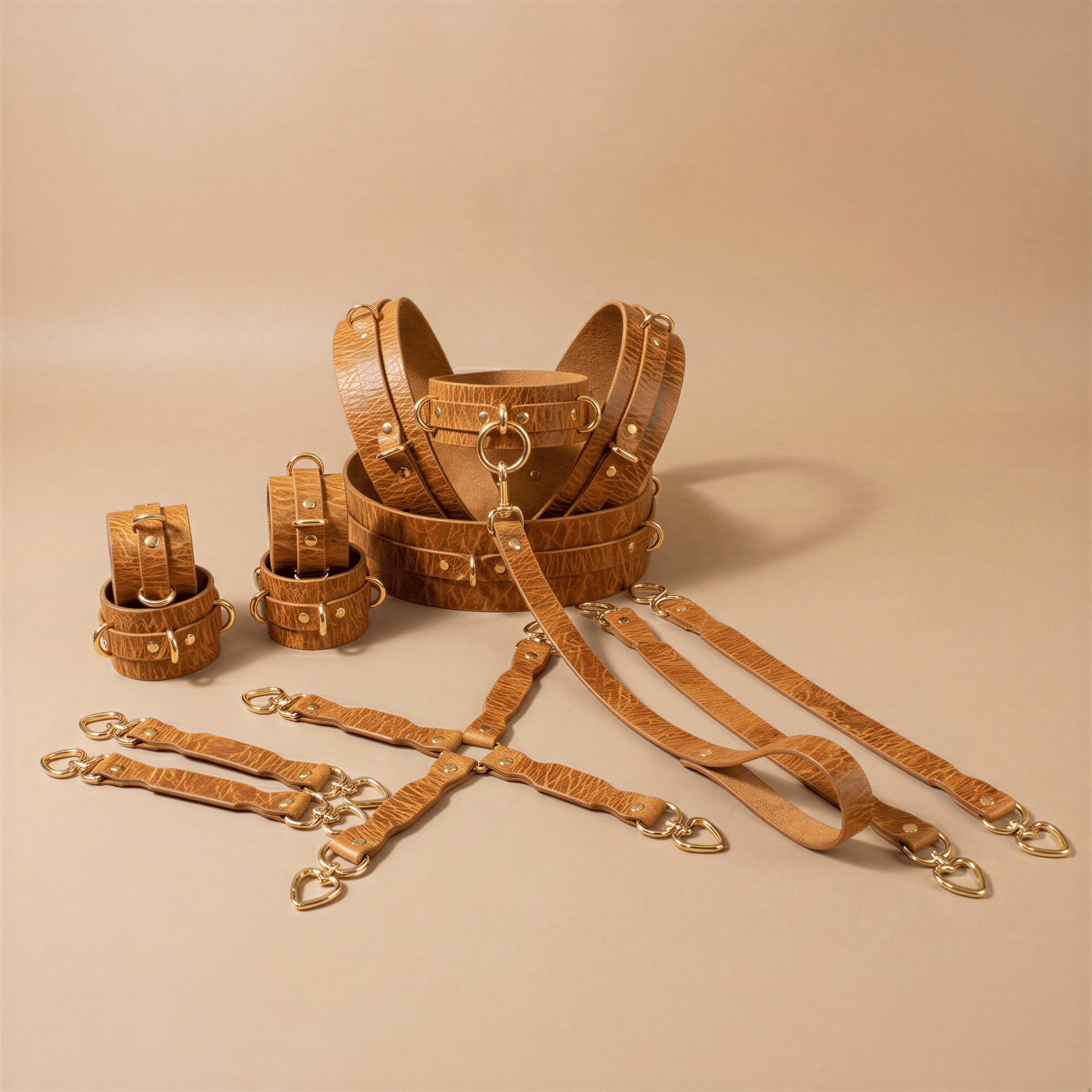 a collection of leather straps and buckles, likely used for BDSM or role-playing purposes. The straps are arranged in various sizes and shapes, with some having gold-colored buckles and others featuring a more rustic appearance. The image does not contain any text or additional objects, and the focus is solely on the leather straps and their arrangement.