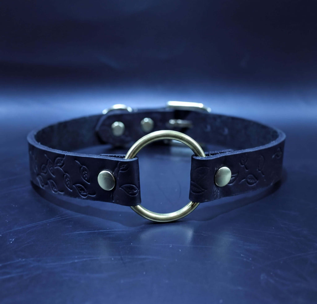 A black leather choker necklace with a gold-colored circular loop and two metal buckles.