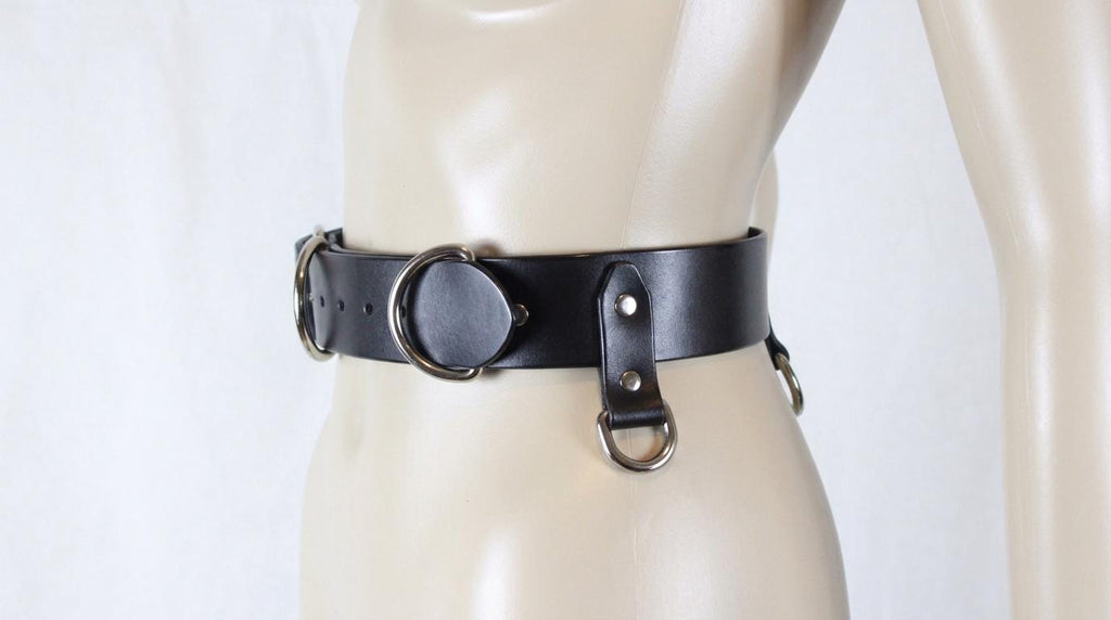 A mannequin wearing a black leather belt with metal rings and buckles.