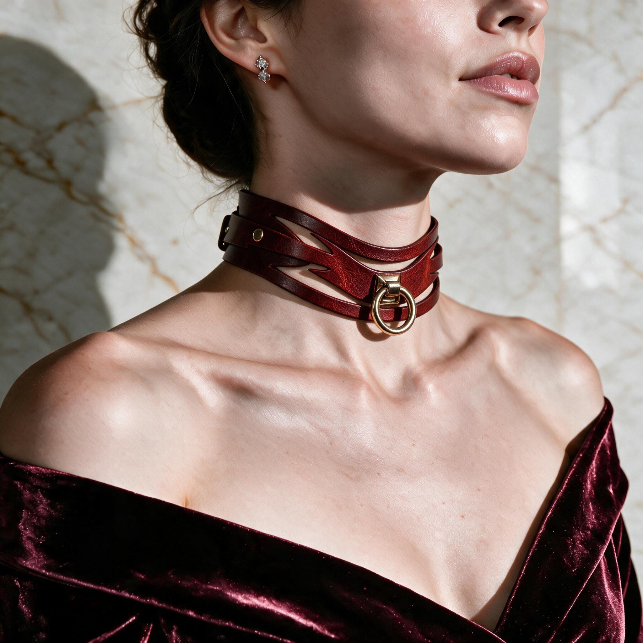 A woman wearing a red choker necklace with a gold buckle, posing against a marble wall.