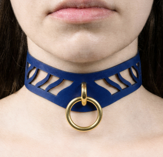 A close-up of a person's neck and chest area wearing a blue choker necklace with a gold ring.
