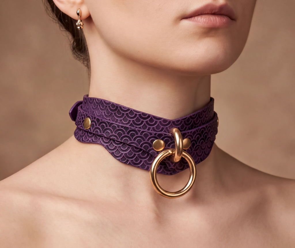 A close-up of a woman's neck and chest area, featuring a purple choker necklace with a gold ring and buckle.