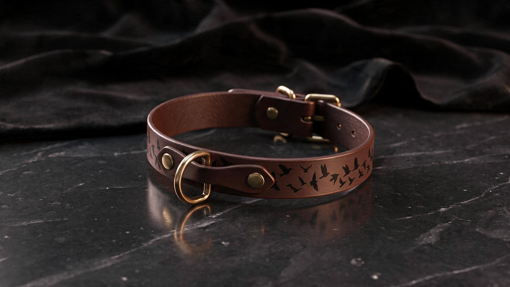 A brown leather collar with a bird design sits on a dark surface.