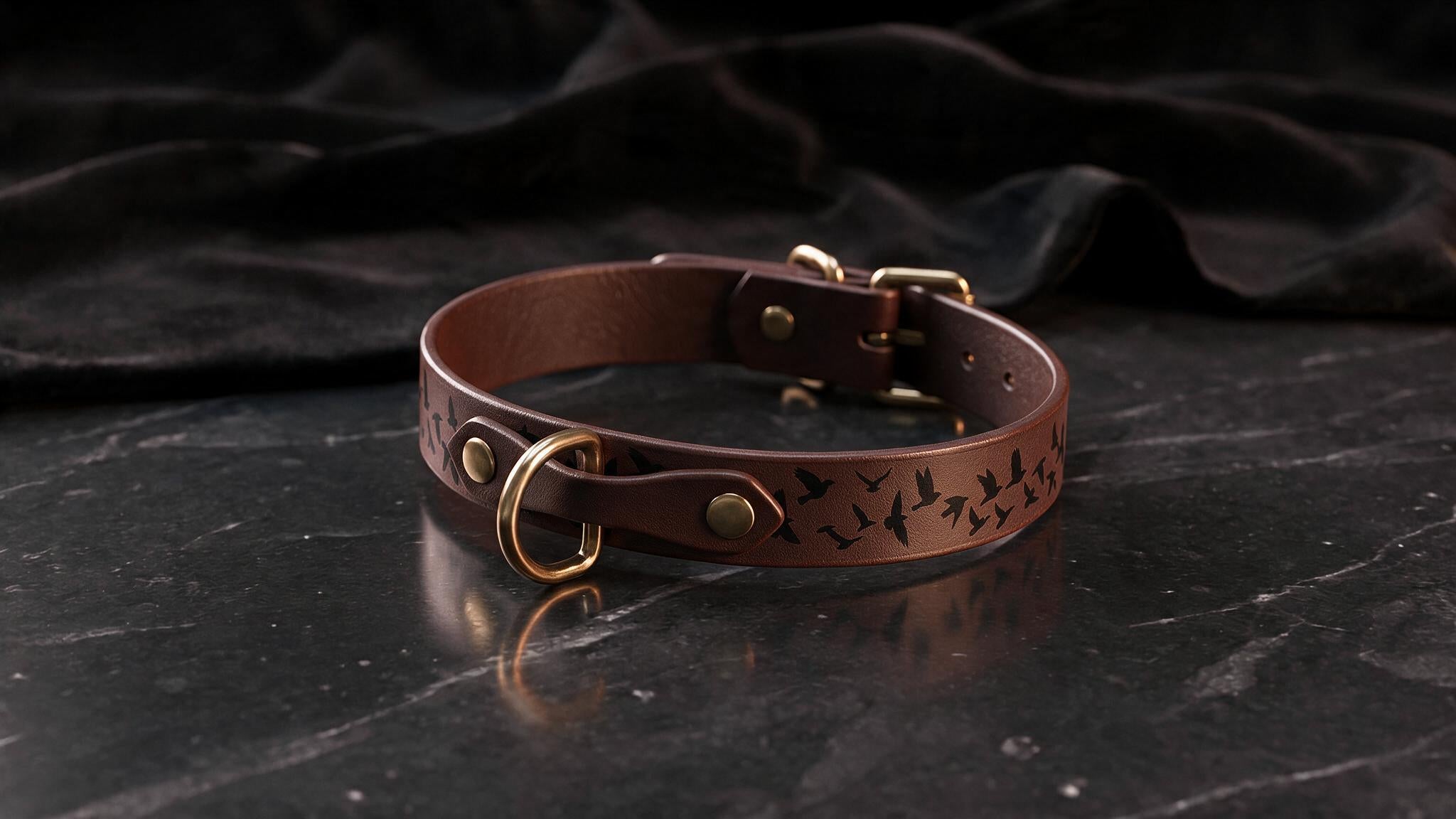 A brown leather collar with a bird design sits on a dark surface.