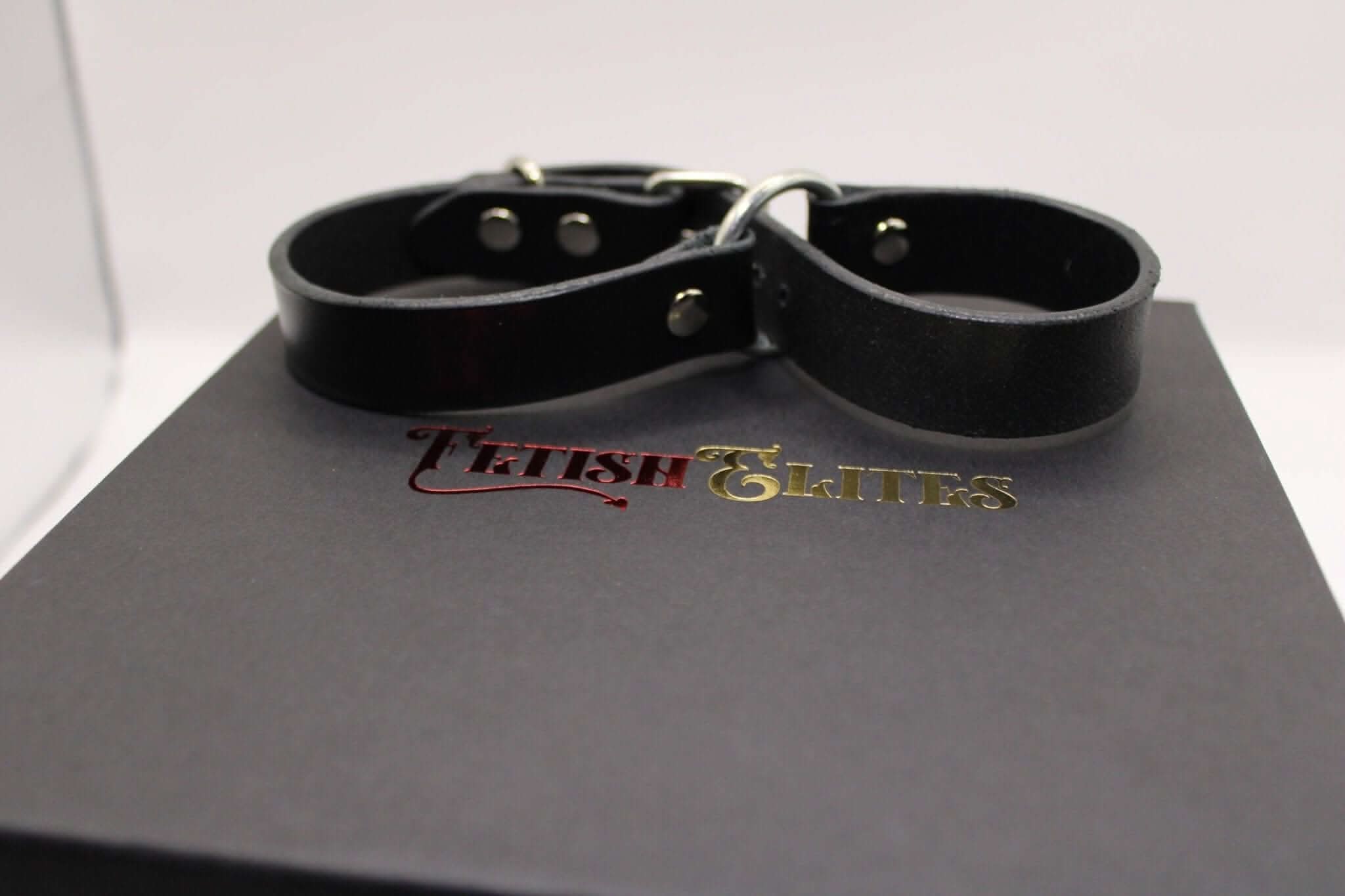 Black leather handcuffs resting on a box, ideal for BDSM, bondage gear, and fetish play for a submissive experience.