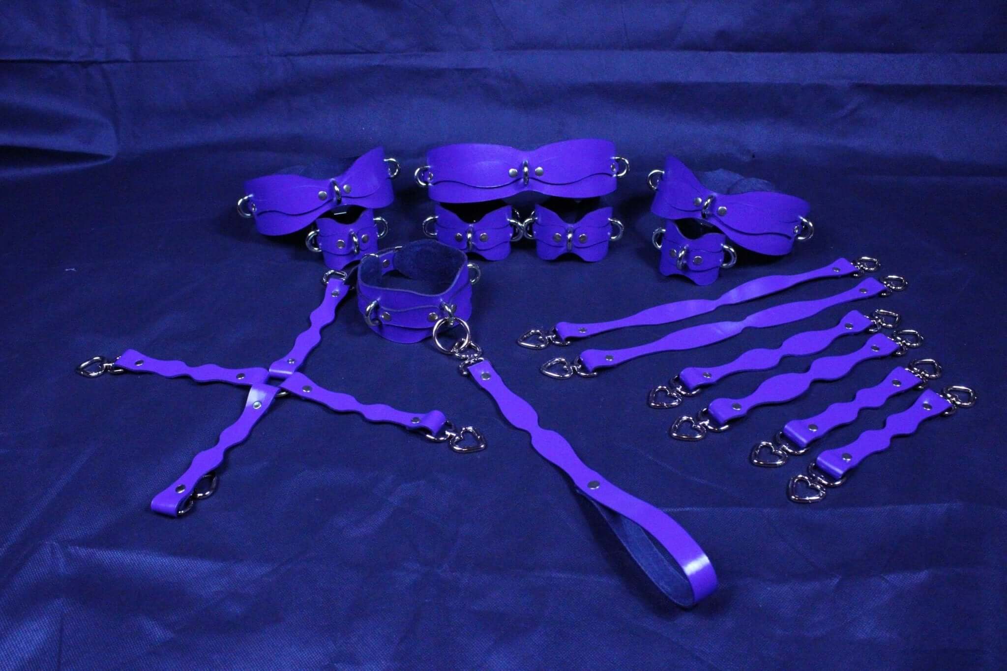 Purple leather bondage kit with collars and cuffs for BDSM play, featuring elegant design and durable construction.