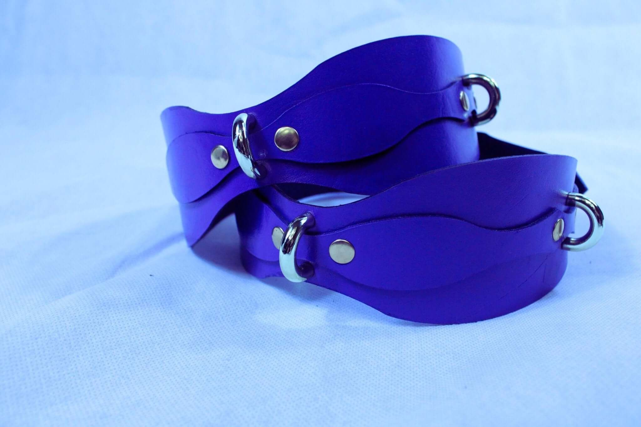 Purple leather restraint cuffs with D-rings for BDSM bondage gear and accessories.