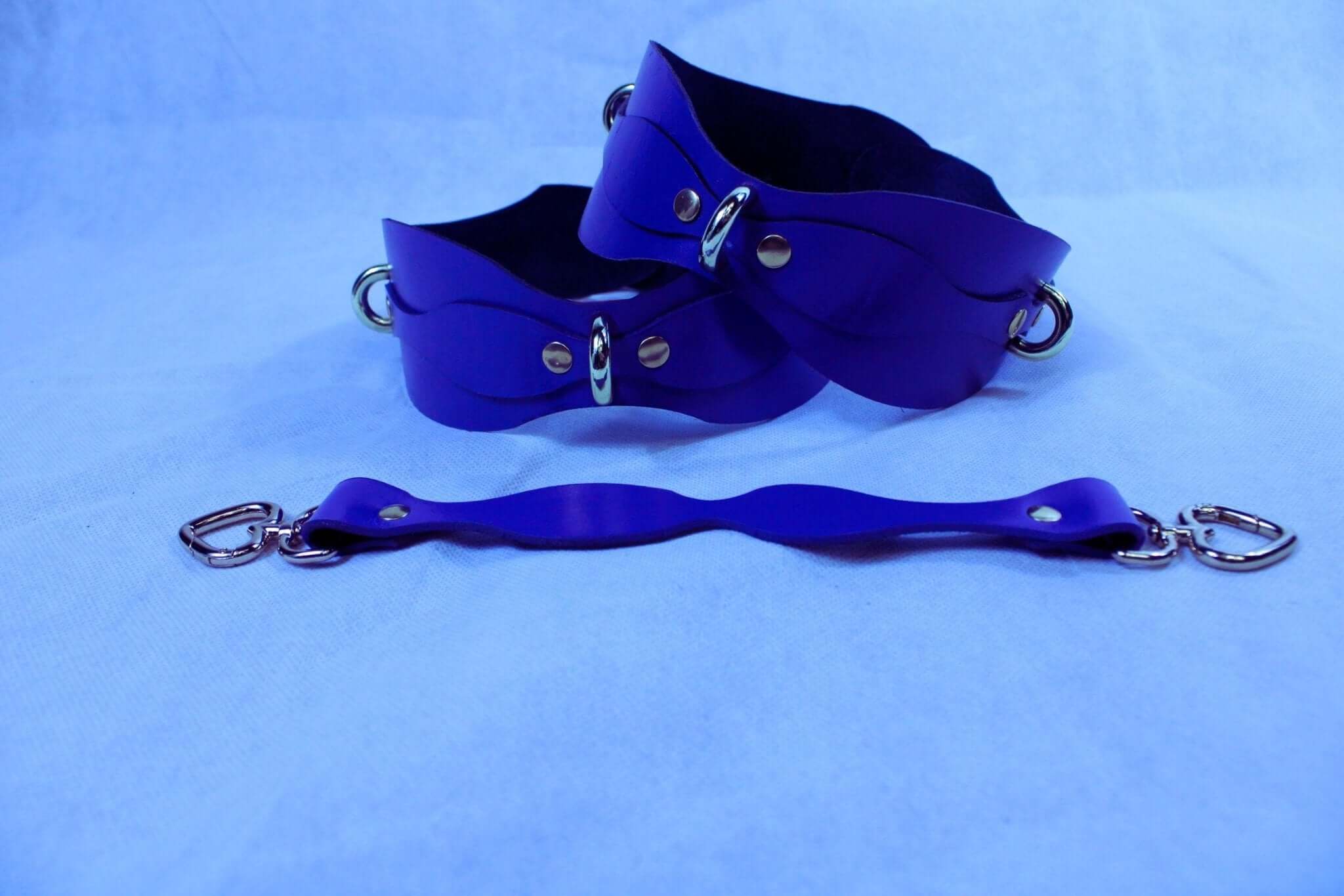 Purple BDSM wrist cuffs with D-rings and connecting strap for bondage gear and restraint play.