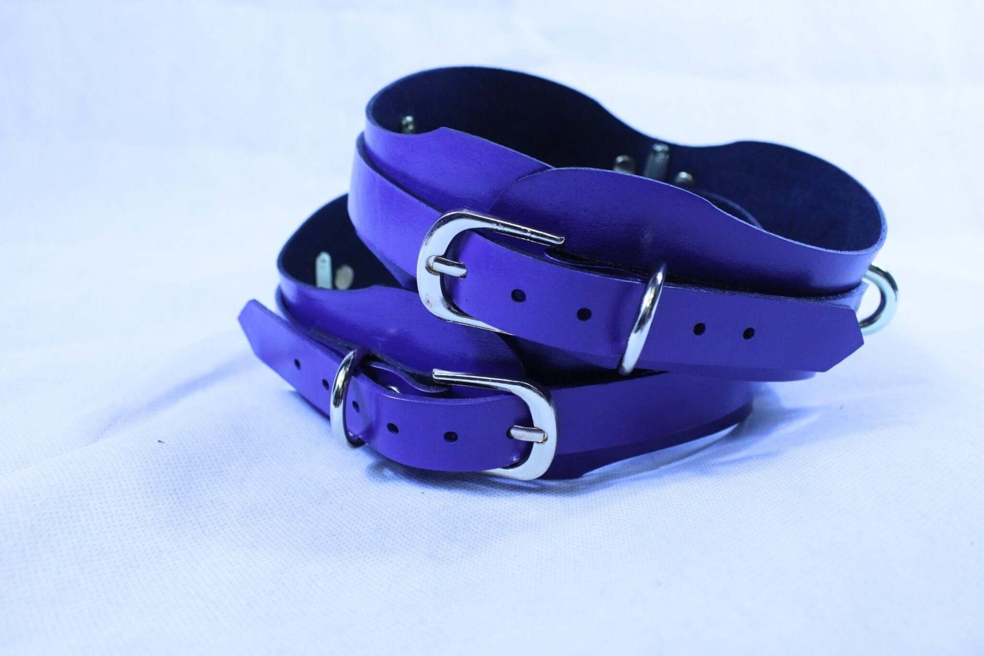 Purple leather thigh cuffs with D-rings, adjustable BDSM gear for bondage enthusiasts.