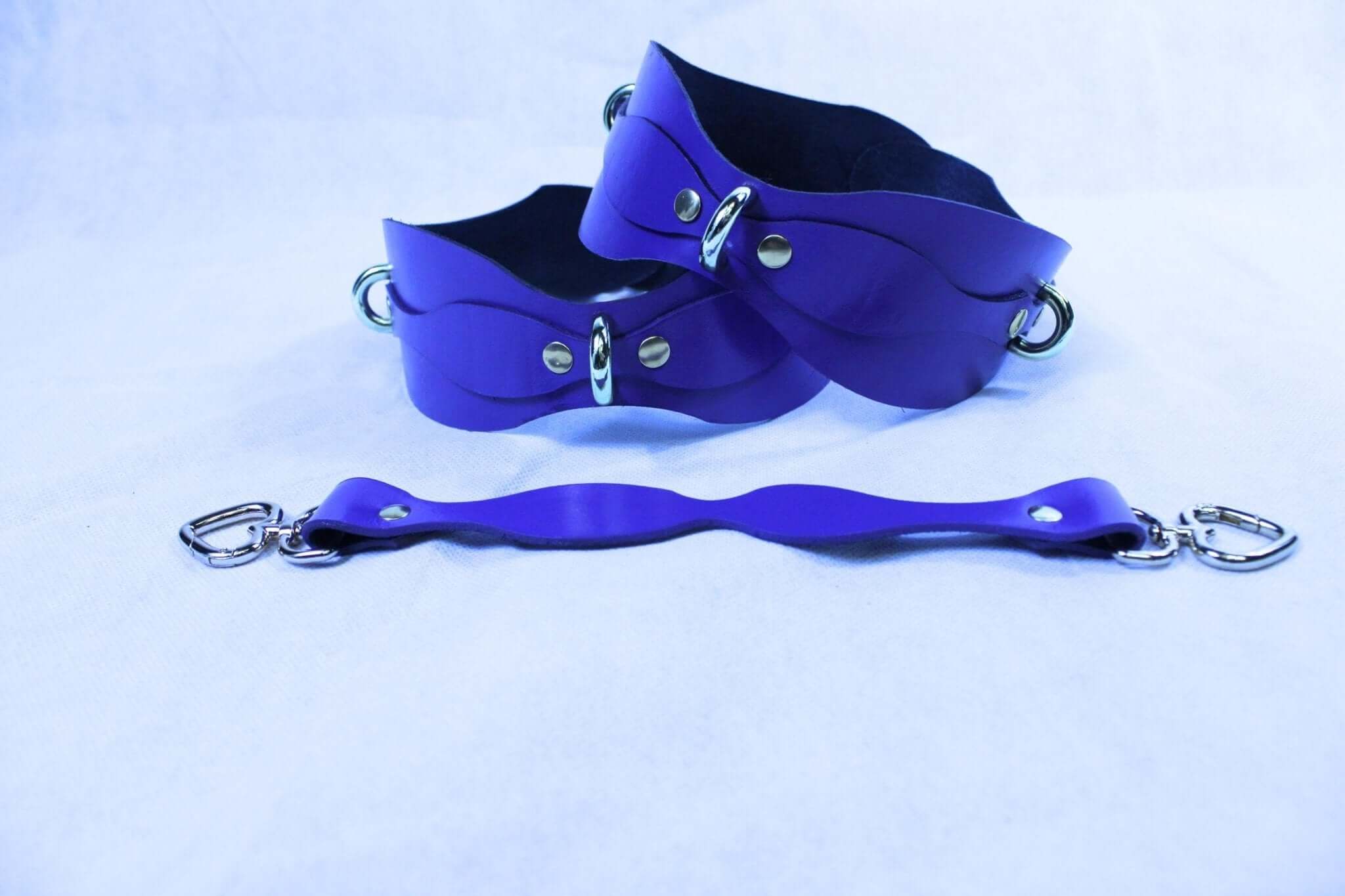 Purple leather thigh cuffs with D-rings and connecting strap, ideal for bondage and BDSM play.