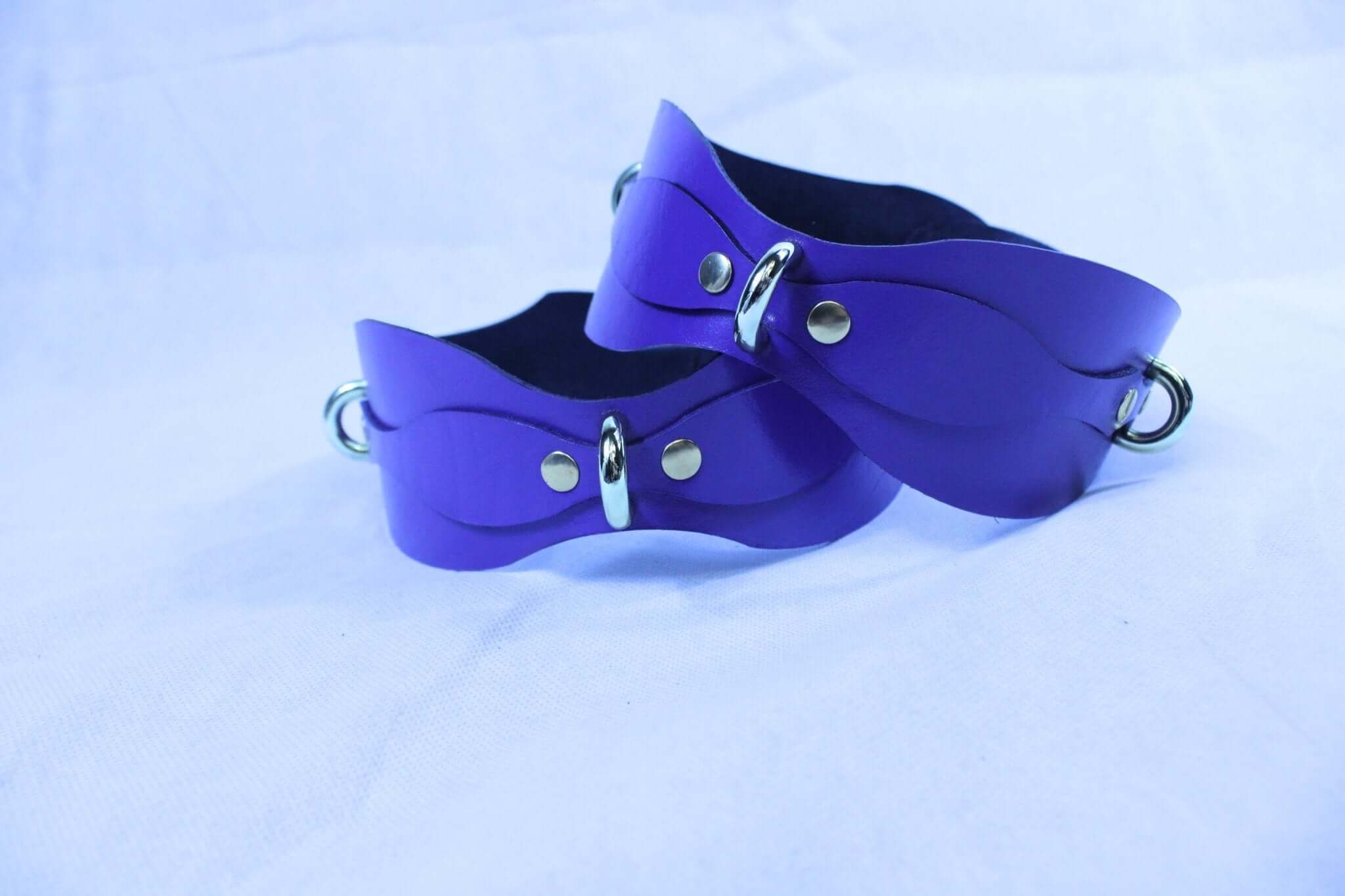 Purple leather thigh cuffs with D-rings, adjustable gear for bondage and fetish lifestyle.