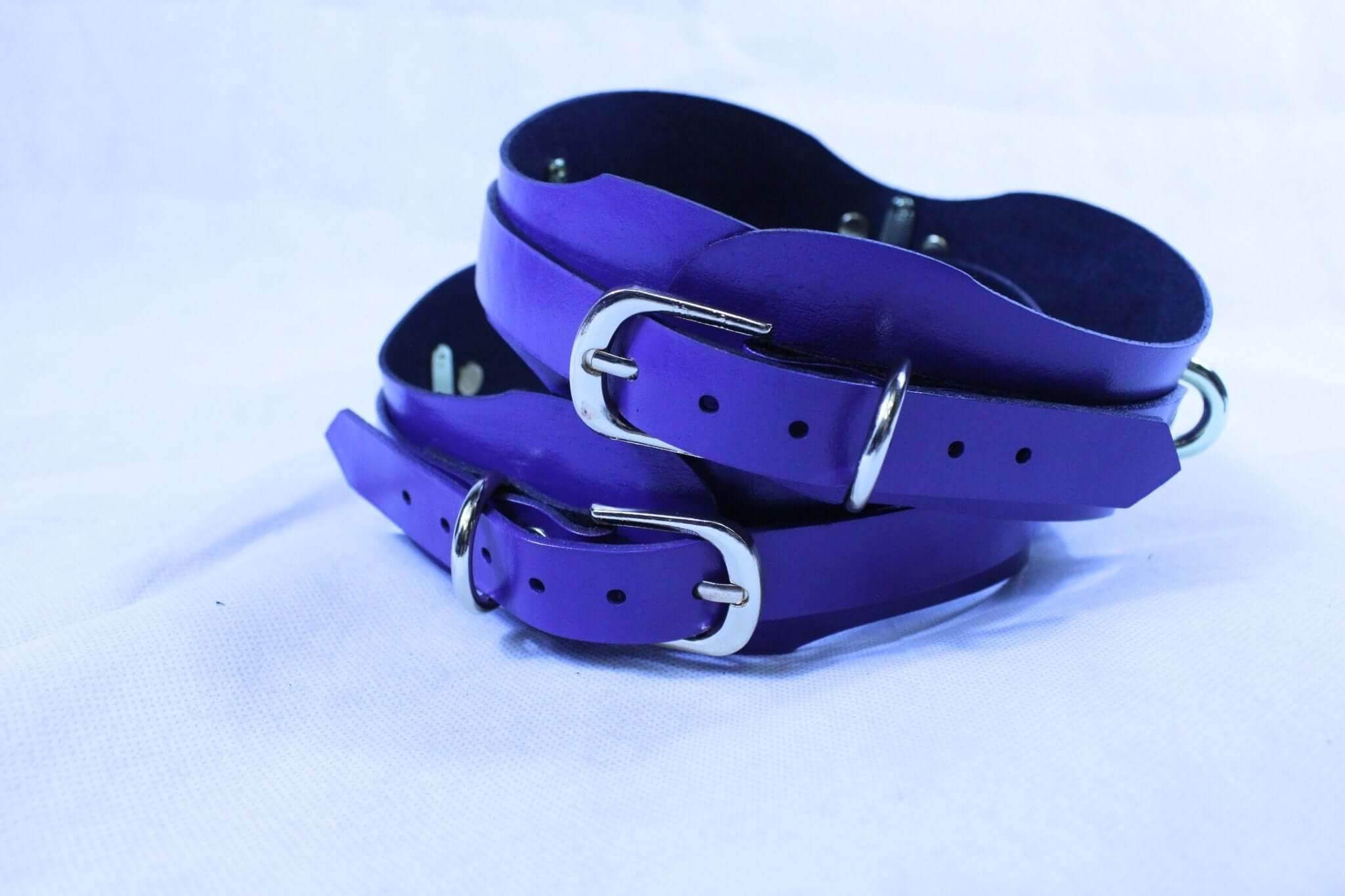 Adjustable purple leather thigh cuffs with D-rings for BDSM and bondage gear, perfect for fetish lifestyles.