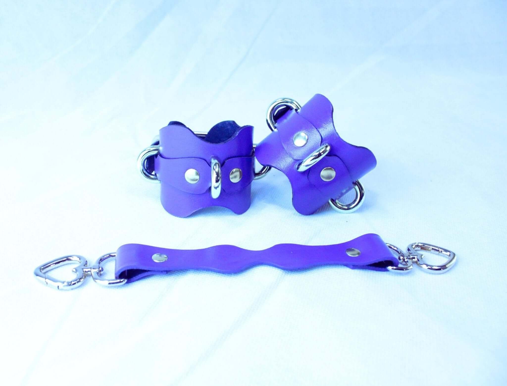 Purple handmade leather wrist cuffs with D-rings, adjustable for BDSM and bondage play.