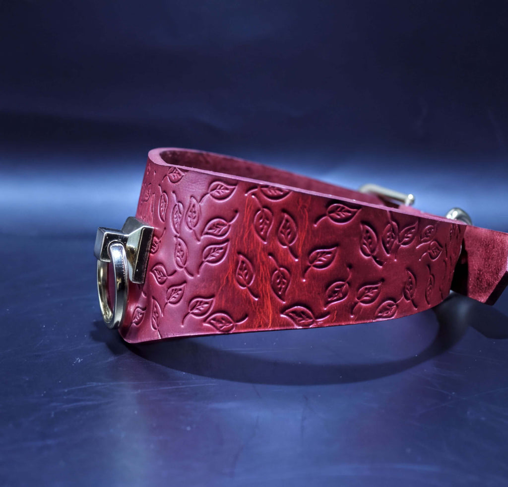 A red leather belt with a leaf pattern embossed on it, featuring a gold-colored buckle.