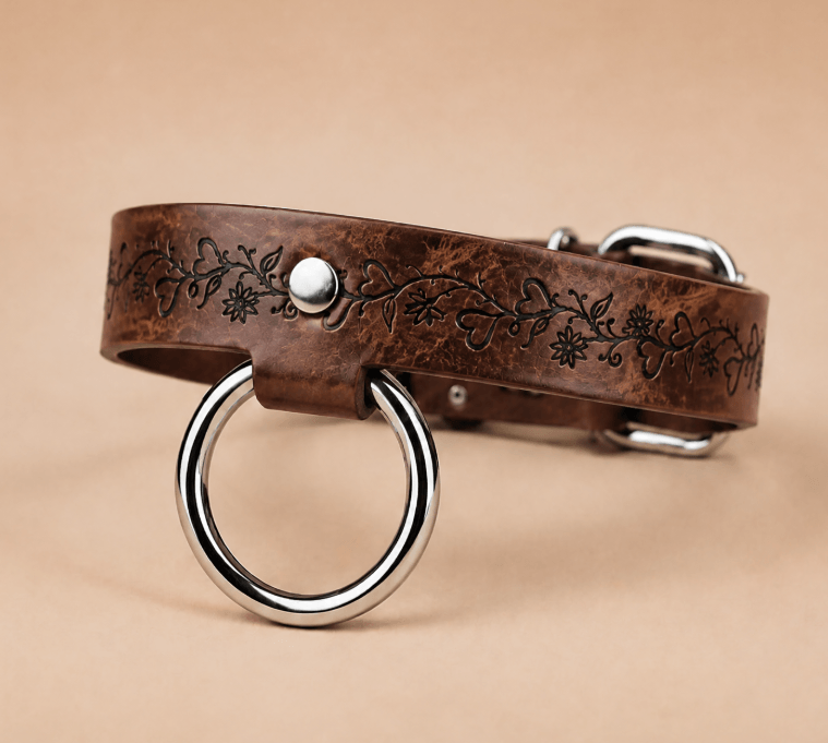 A brown leather dog collar with a metal ring and a decorative floral pattern on the band.