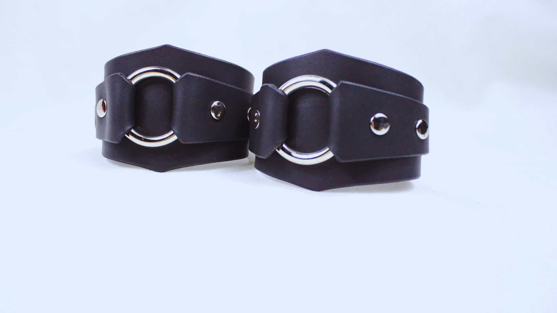 A pair of black leather cuffs with metal rings and buckles, displayed against a white background.