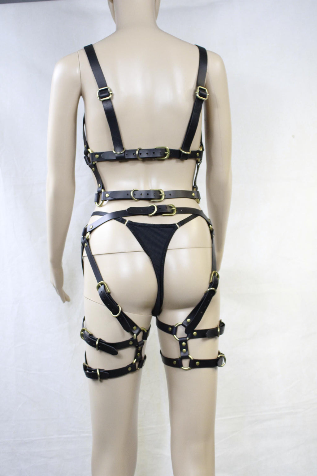 A mannequin wearing a black leather outfit with multiple straps and buckles, including a bra and thigh-high straps.