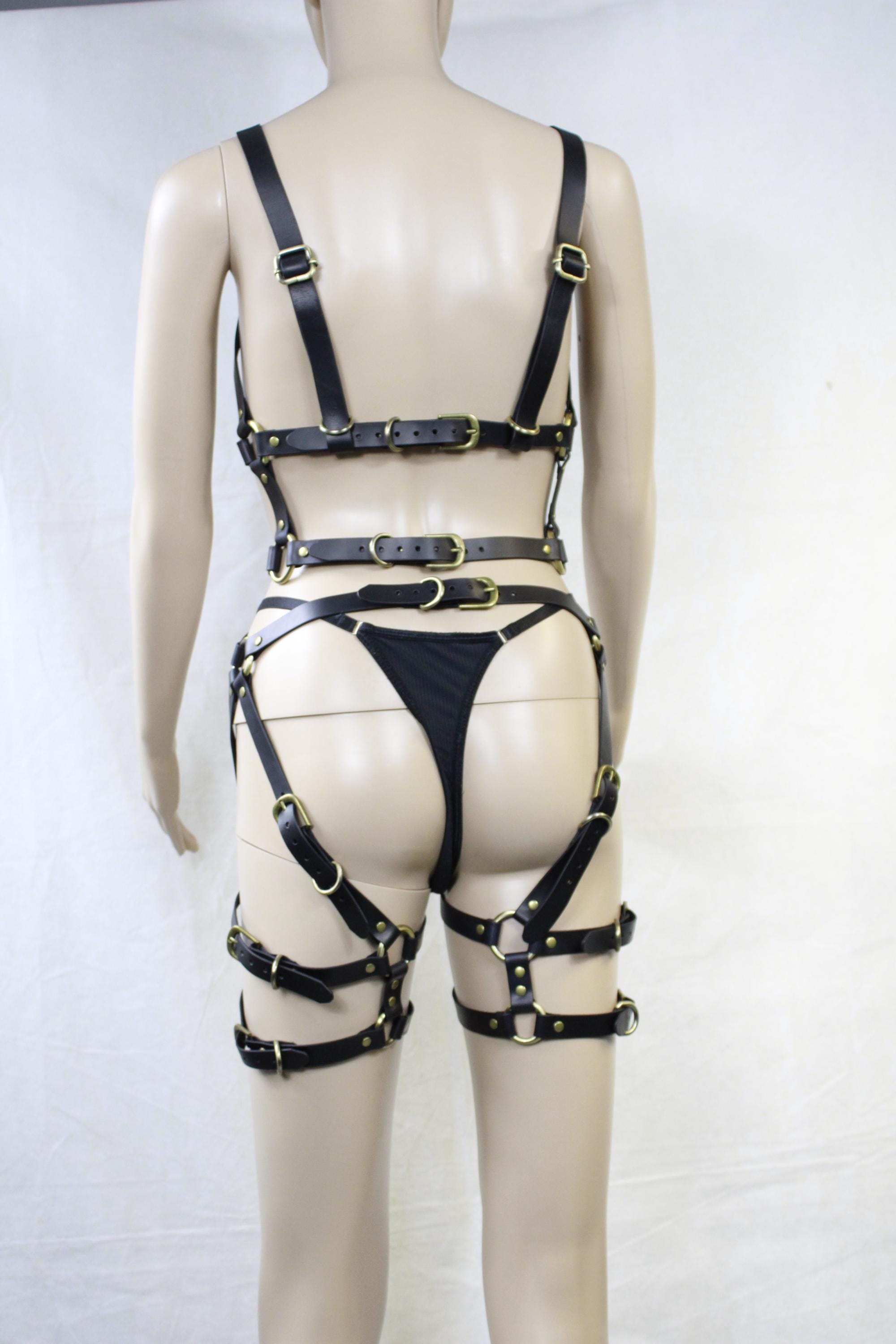 A mannequin wearing a black leather outfit with multiple straps and buckles, including a bra and thigh-high straps.