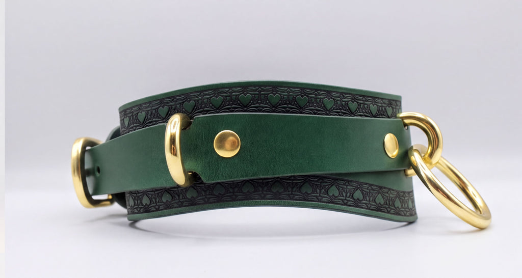 A green leather choker collar with gold hardware, including a buckle and two rings, is shown in the image.