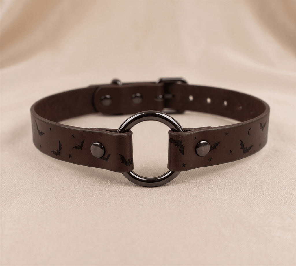 A brown leather choker collar with a circular metal ring and bat-themed design.